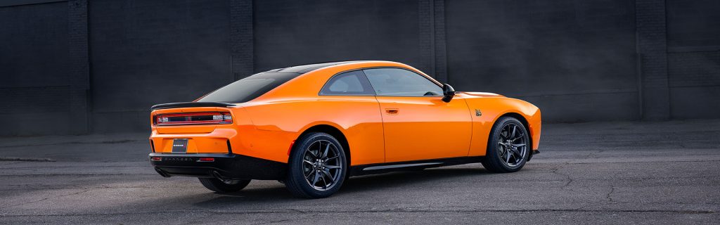 An orange Dodge Charger parked in front of a dark wall.