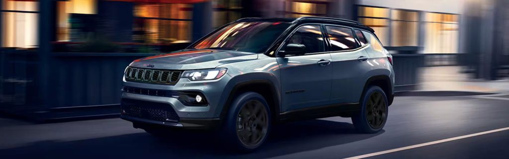 A silver Jeep Compass driving through an urban street at night.