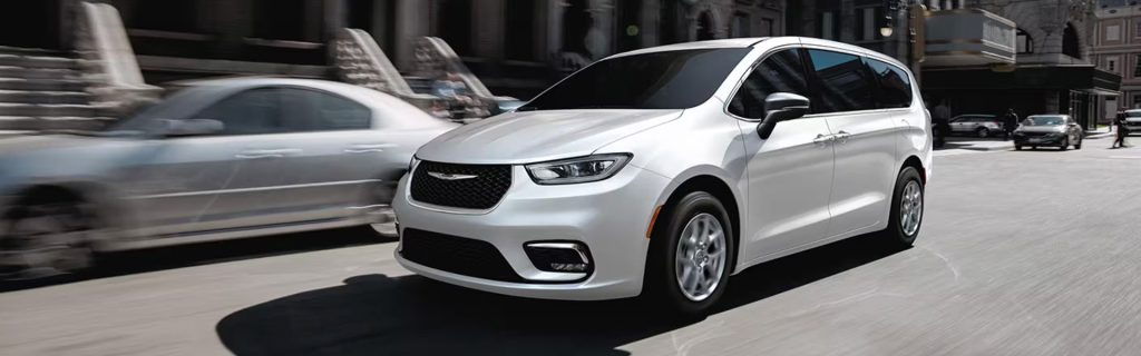 A white Chrysler Pacifica driving through an urban street.