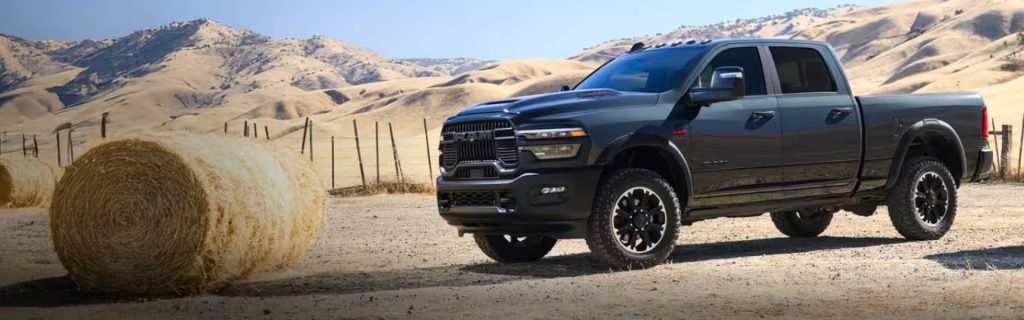 A black RAM 2500 truck parked in a desert landscape next to hay bales.