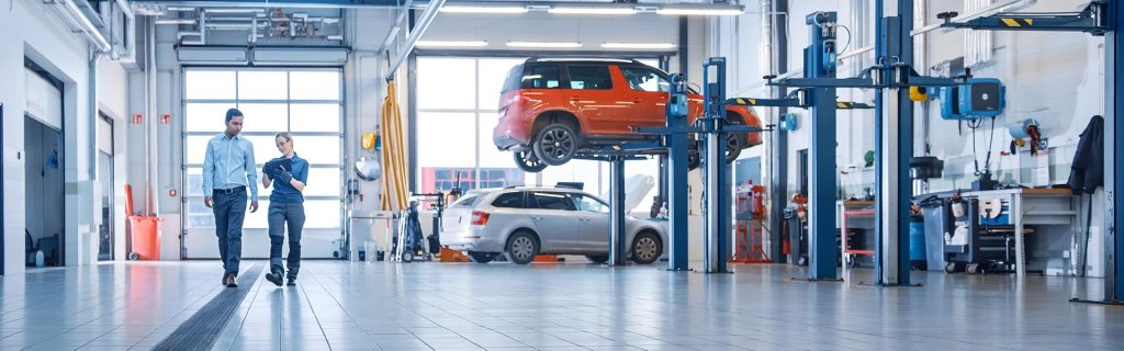 Two people walking through an auto service workshop, with cars on lifts in the background.